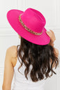 Stylish fuchsia felt fedora hat with a golden chain accent, worn by a woman with long wavy dark hair.