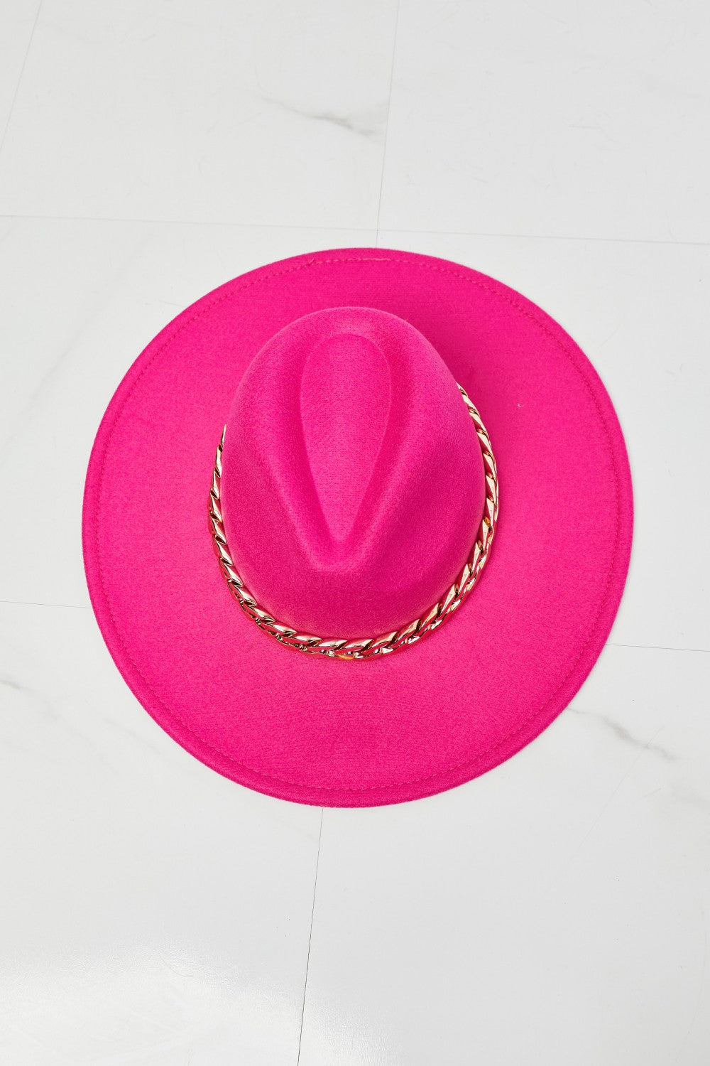 Bright pink felt fedora hat with a gold chain accent, placed on a white background.