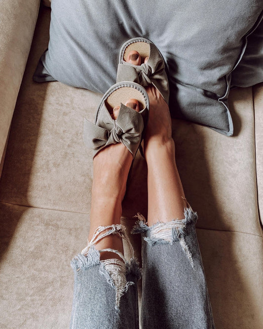 Cozy grey ribbon-tied slippers on a person's feet, against a plain background.